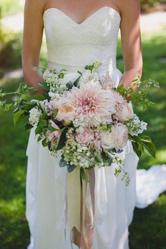 blush wedding bouquets with dahlias and greens in the hands of the bride ameris