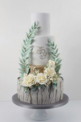 woodland themed wedding cakes bottom layer with gray bark cake white with gold adorned with white flowers and foliage cake trends via instagram