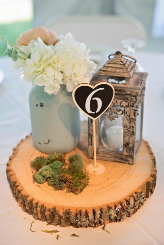 lantern wedding centerpiece on a wooden piece of lantern flowers in a jar of moss and a table number bentley photography via instagram