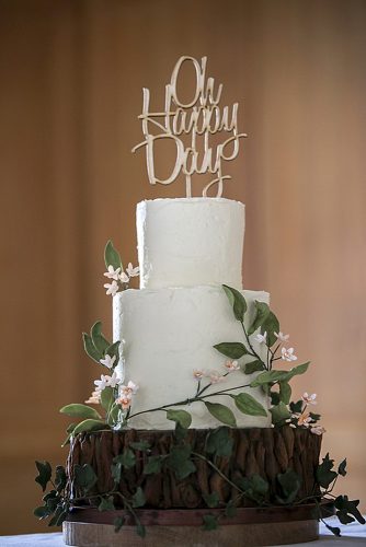 woodland themed wedding cakes white bottom base wooden top with an inscription decorated with green branches with flowers happy hills cakes