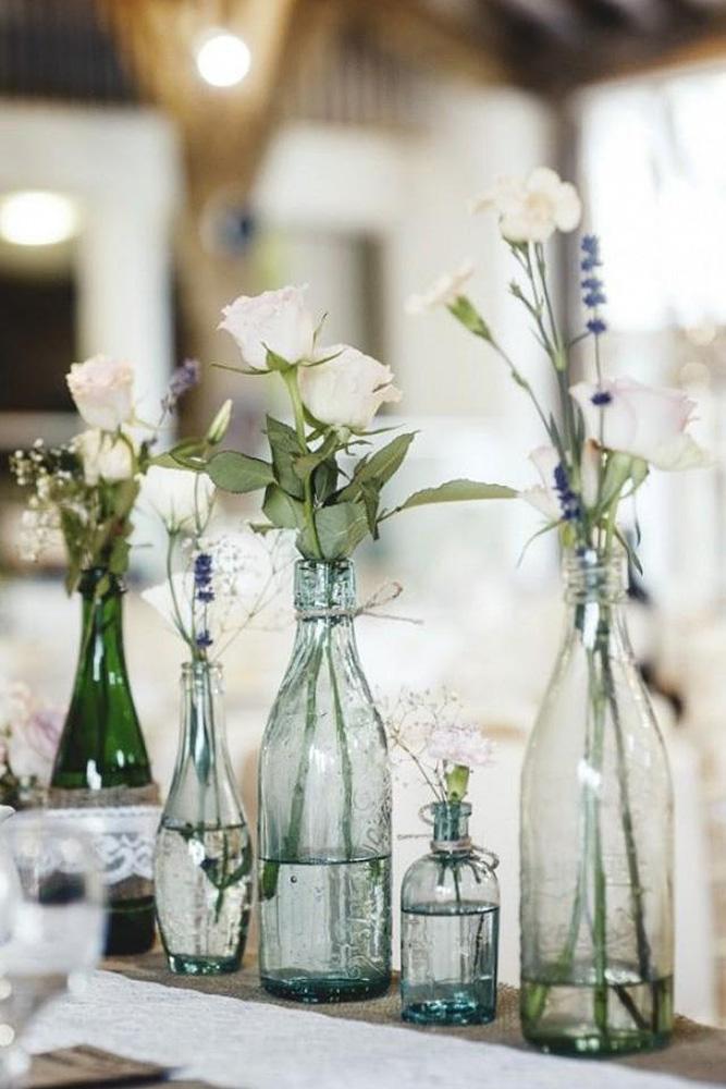 rustic wedding centerpieces white roses in blue glass bottles of different shapes on a linen tablecloth bethany clarke photography
