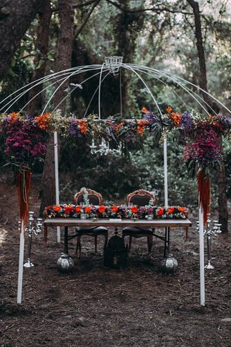 white arbor decorated with flowers dark table and chairs with patterns lorena erre photography