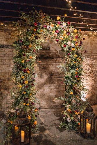 mustard wedding greenry arch with bright flowers and candle lanterns holly clark photography