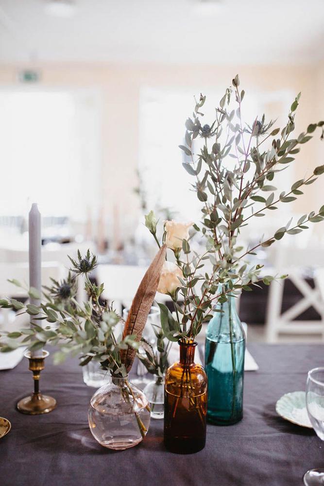 bohemian wedding decorations centerpiece with greenery branch feathers and glass vases and bottles patrick karkkolainen