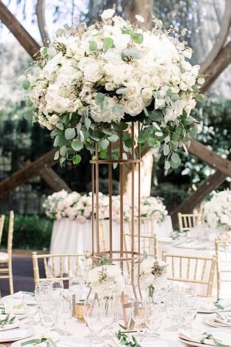 natural wedding décor tall centerpiece with whte flowers and greenery on round table jennyquicksall