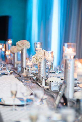 silver wedding decor ideas tablerunner with vaces candles and white flowers on reception with blue lighting natalie franke photography