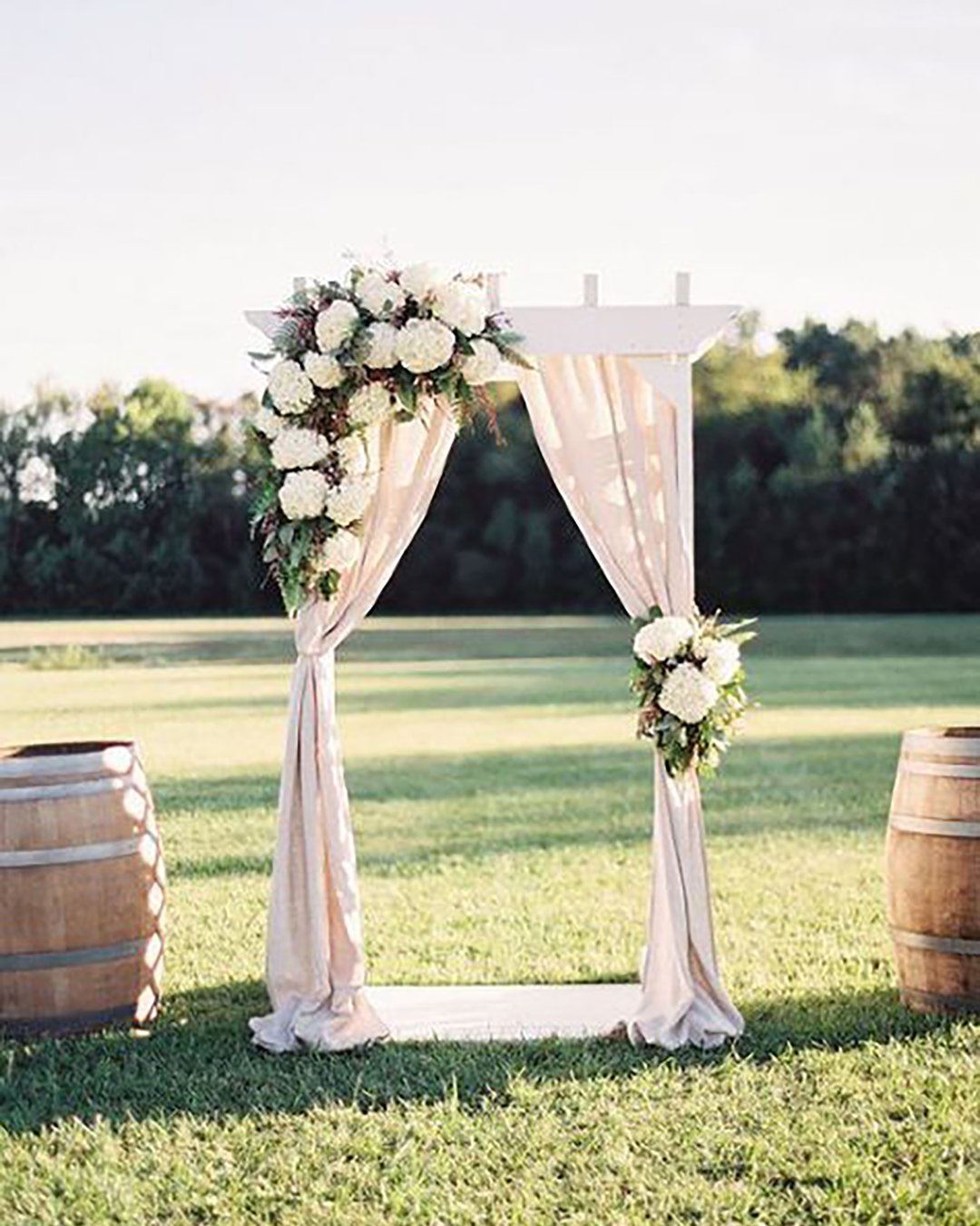 rustic wedding décor white wooden arch decorated with white cloth and flowers surrounded by barrels michael and carina photography