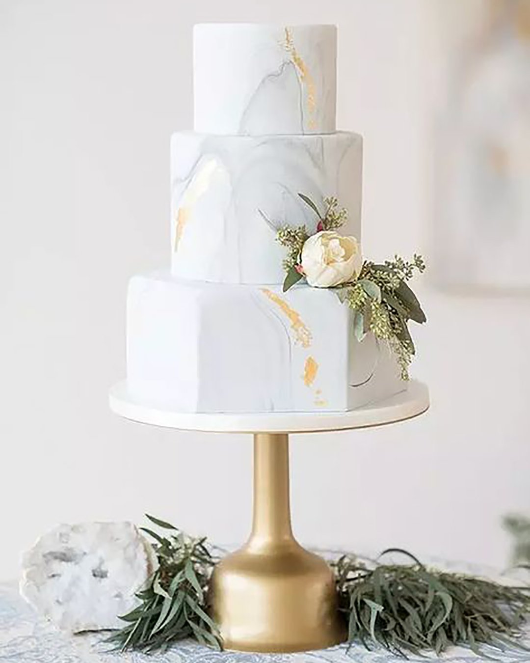 marble wedding cakes three tiered with golden elements and a delicate white flower with greens elegant wedding magazine via instagram