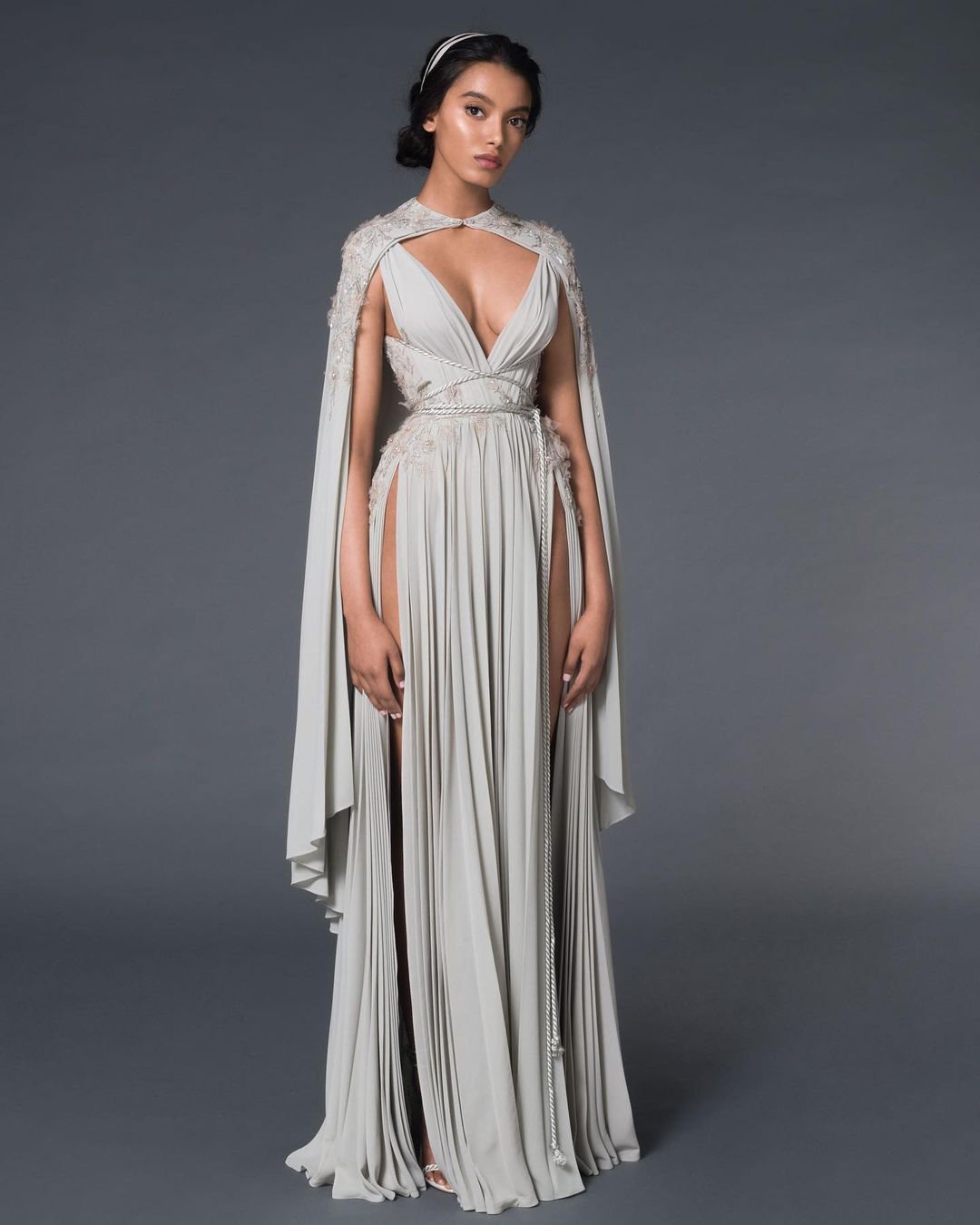 A model wearing an empire-style wedding dress with a cape and v-neckline.